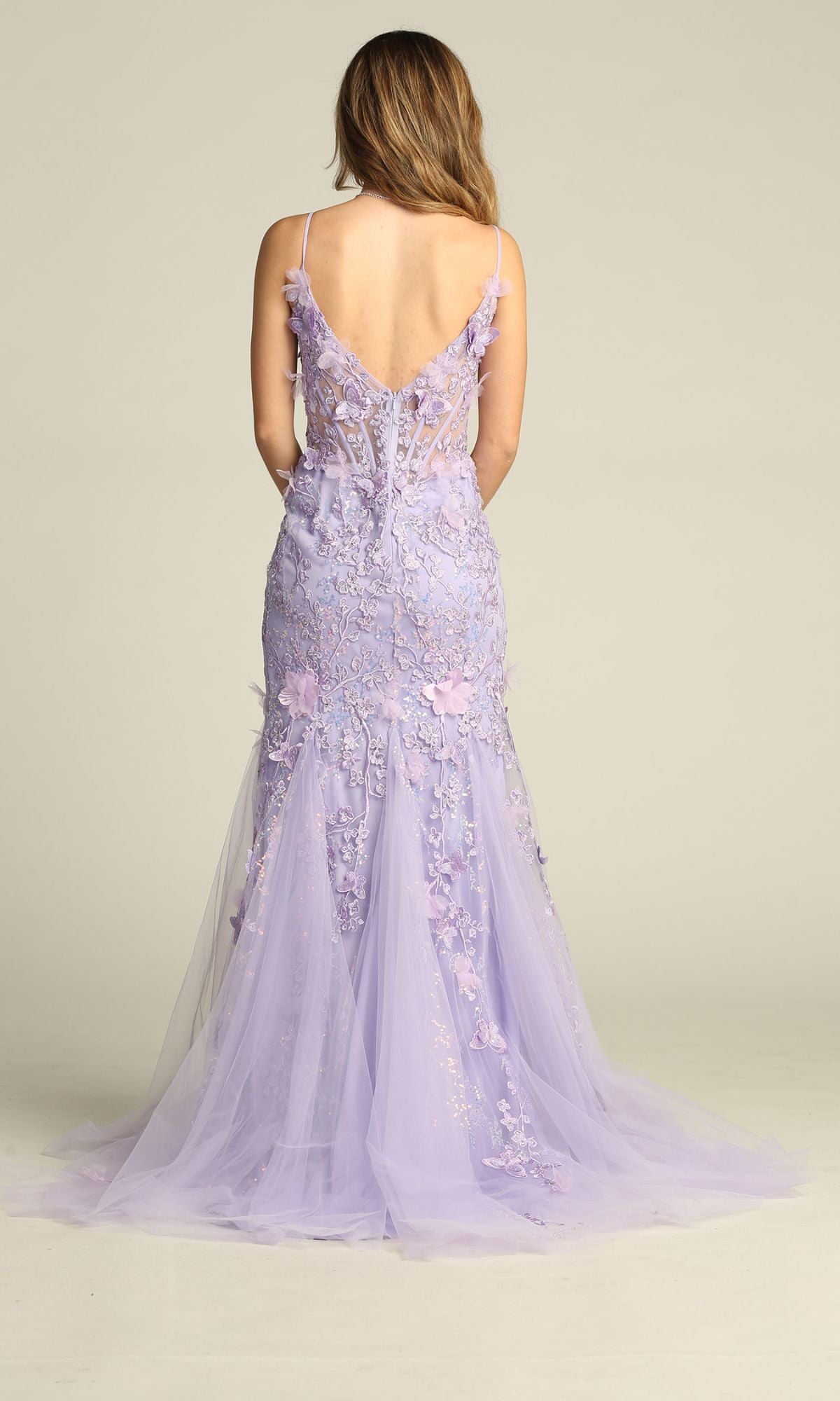 A woman faces away, wearing the Chicas C328 Floral-Embroidered Long Prom Dress, a floor-length lavender gown with lace details and a semi-sheer train.